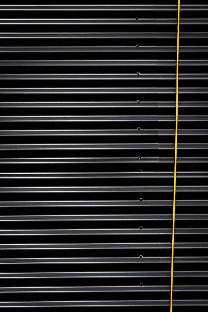 Close-up of a corrugated metal panel with a bold yellow cable, showcasing striped textures and industrial design.